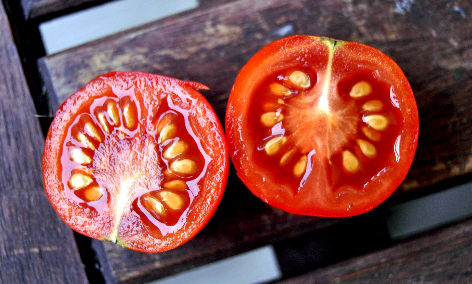 seed saving getting something for nothing image of two halves of a tomato showing the seeds, on a background of wood