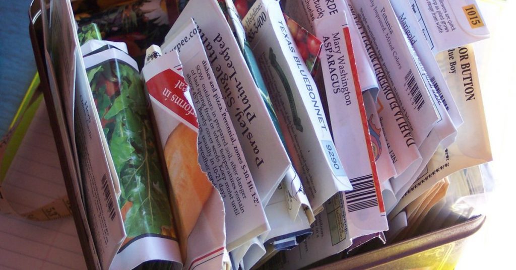 a collection of opened seed packets stored in a metal tin